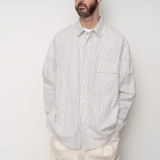 Homme portant une chemise oversize rayée blanche de Still By Hand, collection SS25, avec un style décontracté.