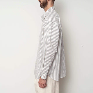 Profil de l'homme en chemise oversize rayée blanche de Still By Hand, collection SS25, mettant l'accent sur le style décontracté.