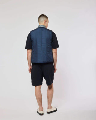 Vue arrière du modèle avec la veste sans manches Homecore - Repeat - Navy, mettant en avant le design minimaliste de la collection SS25.