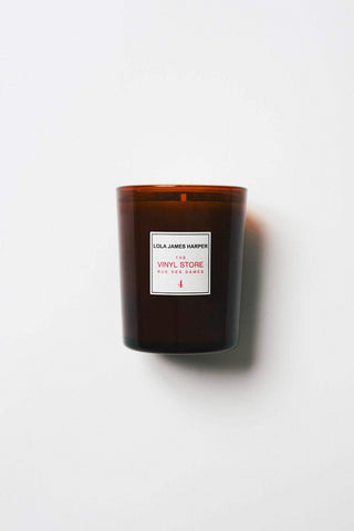 Bougie parfumée de Lola James Harper, intitulée '4. Vinyl store - 190g', présentée dans un verre opaque brun. L'étiquette est blanche avec des inscriptions rouges pour le titre et le nom du vendeur. Idéale pour créer une ambiance chaleureuse.