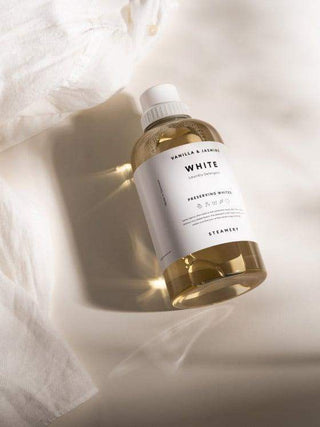 Détergent à lessive blanche de Steamery sur un tissu blanc, mettant en avant la bouteille avec une lumière douce et une ambiance élégante.