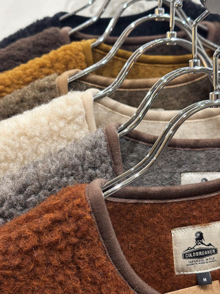 Collection de vêtements en laine de la marque Coldbreaker, mettant en avant des siamois de différentes couleurs, accrochés sur des cintres, illustrant l'authenticité et la qualité de la laine naturelle de Coldbreaker.