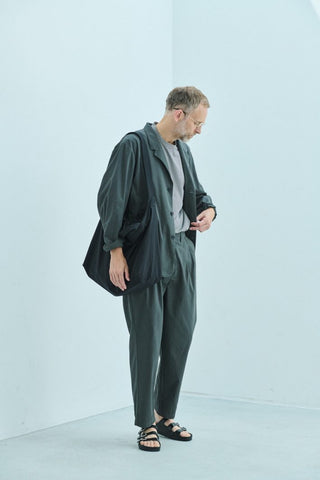 Modèle masculin portant un gilet matelassé bleu marine de la collection Still By Hand, associé à un pantalon ample et une chemise blanche, illustrant le style minimaliste de la collection still by hand ss25.