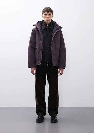 Un homme portant une veste Norse Project en suédine verte, un pull tricoté et un bonnet marron, se penchant légèrement dans un cadre minimaliste. Découvrez le style unique de la collection Norse Project, alliant élégance scandinave et confort.