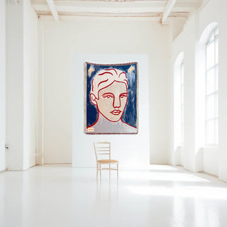 Une pièce de la collection Encré. mettant en avant un mur blanc avec une œuvre d'art moderne représentant un visage stylisé, accompagnée d'une chaise en bois. Un espace lumineux et minimaliste qui illustre l'esprit créatif de la collection.