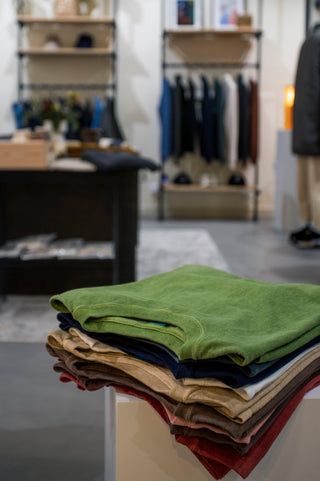 Une pile de T-shirts colorés, y compris un T-shirt vert, dans un magasin moderne qui met en avant les T-shirts & Polos. Découvrez notre collection de T-shirts & Polos alliant confort et style.