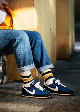Chaussettes Rototo aux couleurs vives, avec des rayures bleues, rouges et jaunes, posées sur une surface en bois. Parfaites pour un look décontracté, ces chaussettes combinent style et confort typiques de la marque japonaise Rototo.