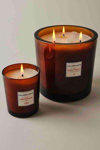 Des bougies parfumées Lola James Harper, dont une plus petite avec l'étiquette 'RUE SAINT-HONORÉ AIR' et une plus grande étiquetée 'THE MUSIC STUDIO ON TRUFO STREET', allumées et créant une ambiance chaleureuse.