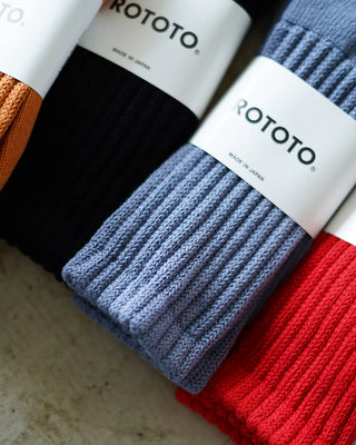 Chaussettes Rototo aux couleurs vives, avec des rayures bleues, rouges et jaunes, posées sur une surface en bois. Parfaites pour un look décontracté, ces chaussettes combinent style et confort typiques de la marque japonaise Rototo.