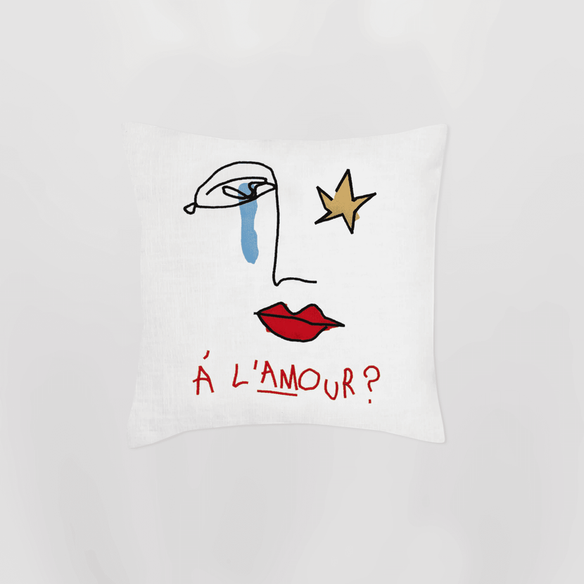 Coussin brodé "A l'amour?" - White de la marque Encré, présentant une illustration artistique avec des lèvres rouges, une étoile dorée et un œil avec une larme bleue sur fond blanc.
