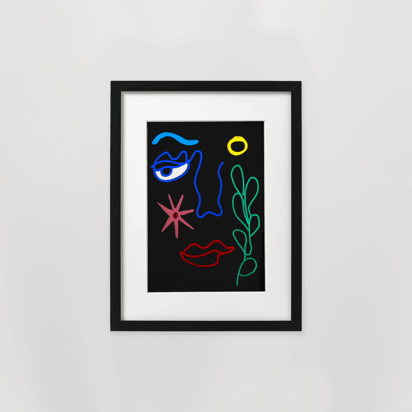 Œuvre d'art contemporaine enbrodée représentant un visage avec des motifs colorés sur fond noir, présentée dans un cadre noir. Cadre brodé "Aqua" - Black par Encré.