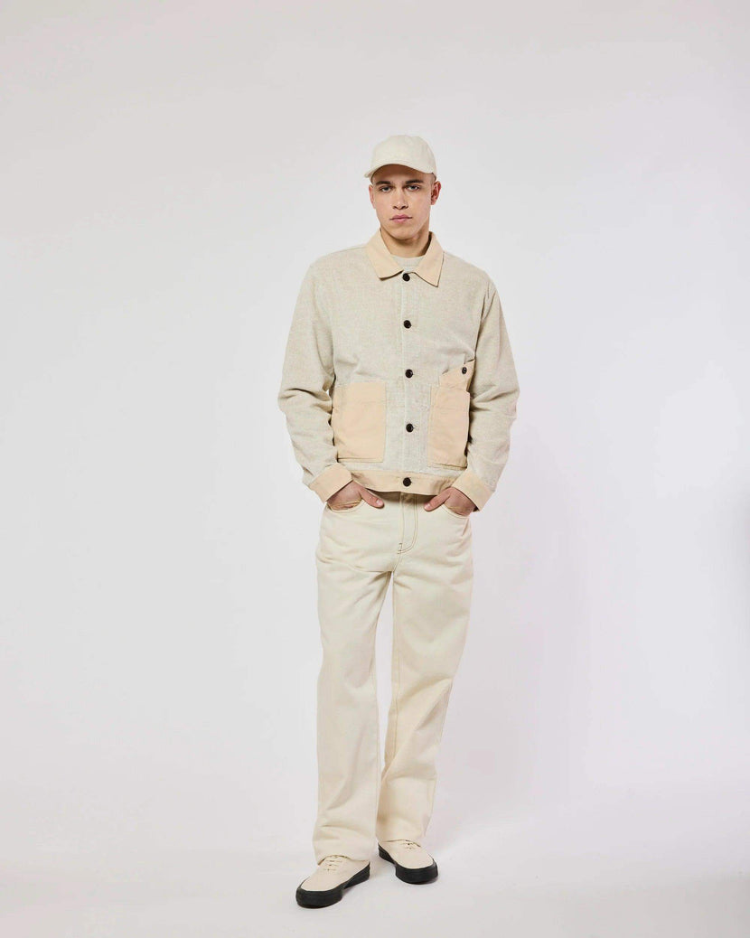 Modèle portant la veste Dario Tupelin - Ecru de Homecore, avec un design bi-matières en couleur écru et beige, accompagné de pantalons clairs et des chaussures claires.