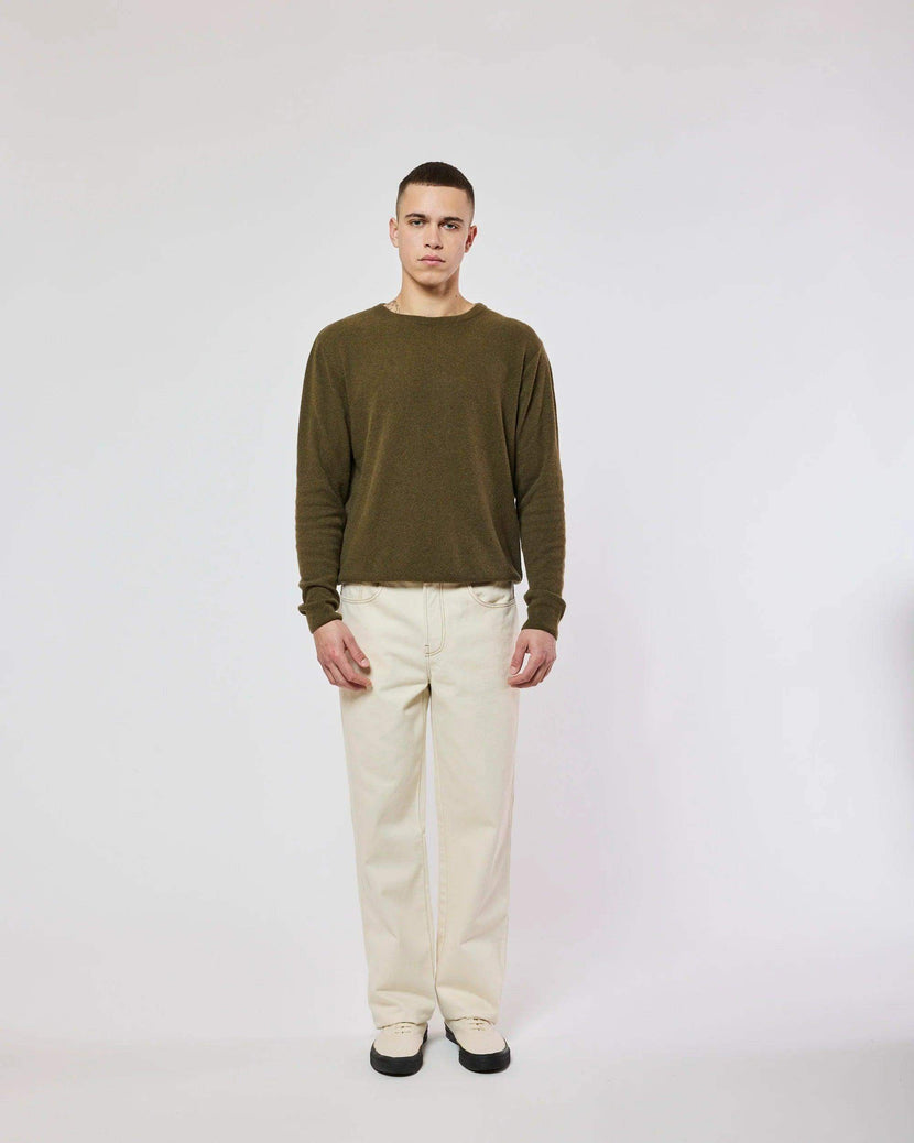Un homme portant un pull Edriss - Khaki de la marque Homecore, avec un pantalon beige. Le pull a une coupe droite et un design simple, parfait pour un look décontracté.