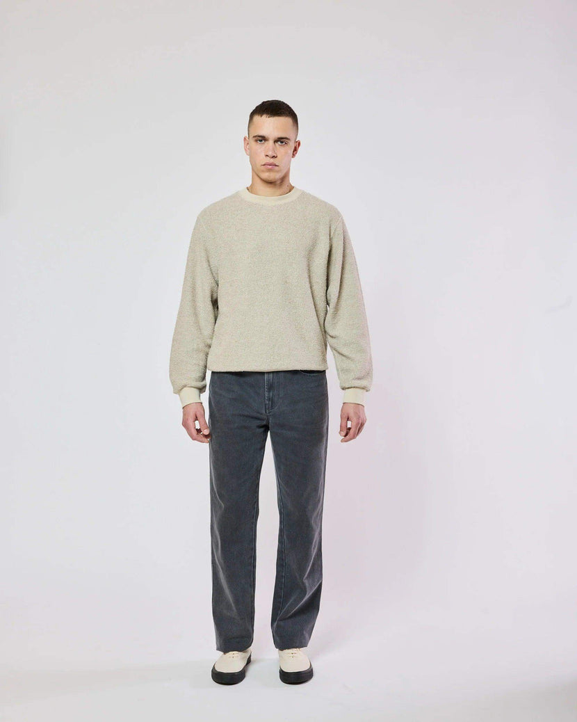 Un homme portant le Mko Hemp Sweat de Homecore, un sweat-shirt en molleton à col rond de coupe oversize, combiné avec un pantalon gris foncé. Le tissu mélange coton et chanvre offrant une sensation douce.