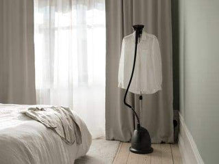 Défroisseur Cumulus Home Steamer de Steamery en utilisation dans une chambre, avec un vêtement suspendu, illustrant son design élégant et pratique.